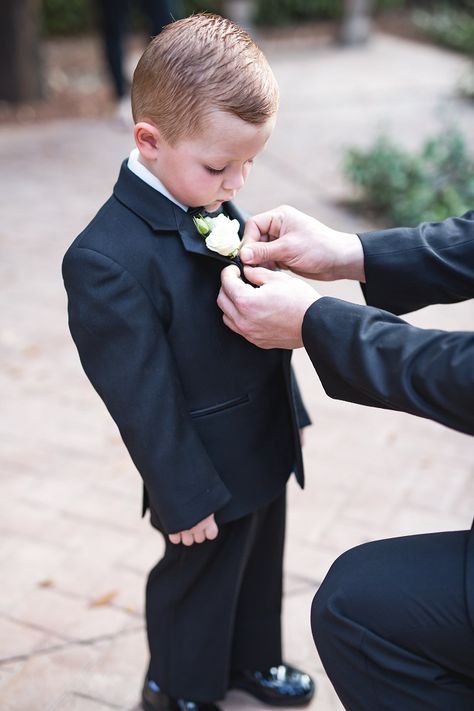 Ring bearer getting his white rose boutonniere pinned on his black suit before the wedding ceremony | Lindsay Borg Photography | villasiena.cc Ring Bearer Black Suit, Ring Boy Wedding, Ring Barrer, Spray Roses Boutonniere, Ring Bearer Boutonniere, Ranunculus Boutonniere, White Rose Boutonniere, White Spray Roses, White Boutonniere