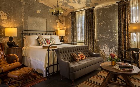 A picture of Hotel Emma's version of a presidential suite, named the Emma Koehler suite. Pictured is the tall ceiling room with king-sized white bed with a grey couch in front of it and a tan chair next to it. Hotel Emma San Antonio, Hotel Emma, Antique Iron Beds, Iron Beds, Rose House, Iron Bed, Luxury Suite, Antique Iron, Hotel Collection