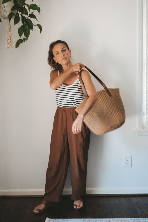 ashley wearing a white and navy striped top, brown drapey pants, brown leather sandals, a tan woven tote bag, and tan frame sunglasses Pop Of Color Outfits Casual, Boho Mom Outfits, Striped Tank Top Outfit, Goal Outfits, Brown Linen Pants, 2024 Clothes, Minimalist Fashion Summer, Mom Style Summer, Curated Wardrobe