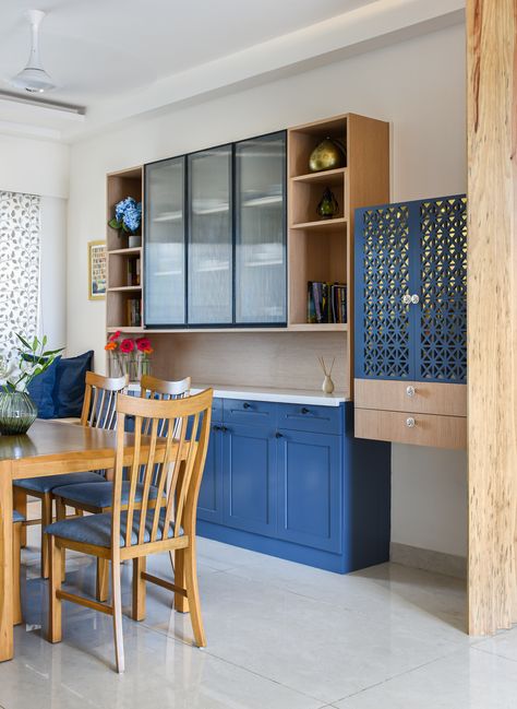 Step into a dining room that balances elegance with vibrant energy. A grand wooden shelving unit takes centre stage, boasting compartments concealed behind stylish blue-panelled doors. Adjacent to it, a smaller wall-attached shelving space adds a touch of functional finesse. The chairs, upholstered with blue fabric, complement the wooden six-seater table. Against a backdrop of white marble floors and walls, this space exudes invigorating charm. Credit: propfloorrealty Photo Credit: Nayan Soni Wall Attached Dining Table, 6 Dining Table, Dining Room Display, Dining Table Set For 6, Dining Table For 6, Wooden Shelving, Panelled Doors, White Marble Floor, 6 Seater Dining Table