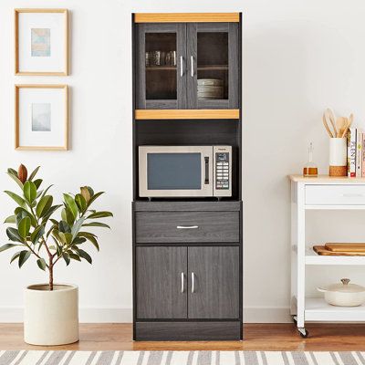 This simple yet versatile piece is sure to add functionality to your kitchen. Standing tall, this unit has a large open shelf space in the center for your microwave or oven. The transparent door at the top opens to reveal two shelves, perfect for displaying fine tableware. For extra storage, there is an enclosed cabinet underneath for small appliances, pots and pans. A single drawer in the center of the unit provides ample space for utensils, kitchen towels and other gadgets. So go ahead and bri Crockery Unit With Microwave, Kitchen Cabinet Tall Unit, Microwave And Oven Cabinet Kitchen Ideas, Kitchen Units Ideas Small Spaces, Kitchen Stands Ideas, Simple Kitchen Cabinet Design Ideas, Oven Stand In Kitchen, Microwave Unit In Kitchen, Tall Units In Kitchen Storage