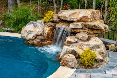 Make your pool more exciting with a cool water feature, like this rock waterfall. Whether you prefer modern or natural, we can help create your perfect pool for your backyard. Outdoor Pool Waterfalls, Rock Pool Waterfall, Square Pool With Waterfall, Waterfall In Pool Backyards, Fiberglass Pool With Waterfall, Rock Feature Pool, Waterfall Pool Backyard, Above Ground Pool With Waterfall, Small Pool Waterfall