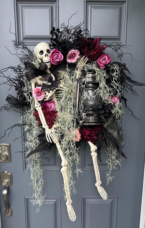 Welcome the spooky season with this stunning Halloween eerie skeleton front door wreath adorned with delicate pink roses, eerie creepy moss, and whimsical lantern LED light that will light up your entrance with a mysterious glow. Perfect for adding a touch of charm and spookiness to your home decor, this unique wreath is sure to impress your guests and trick-or-treaters alike. Embrace the Halloween spirit and make a statement with this one-of-a-kind decoration. Skeleton is 36" and is moveable. Lantern does light up! Skeleton Door Decoration, Wreath With Lantern, Halloween Arrangements, Stylish Halloween Decor, Spooky Halloween Crafts, Skeleton Wreath, Unique Wreath, Diy Halloween Wreath, Creepy Halloween Decorations