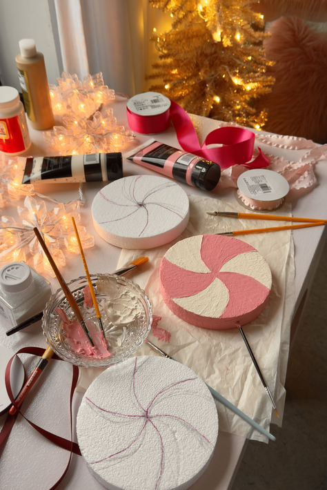 Crafts set up on a pink desk as I prep to start and oversized candy ornament DIY. Styrofoam circles are seen painted in pink and white swirls while paintbrushes, paint, ribbon, and other craft supplies are seen while the craft is in process. Sparkly christmas lights adorn the scene. Diy Pinkmas Decorations, Pink Christmas Porch Decor, Whimsy Christmas Tree, Candy Christmas Aesthetic, White House Decorations, Diy Whimsical Christmas Decor, Pastel Christmas Aesthetic, Oversized Decor, Pink Christmas Diy