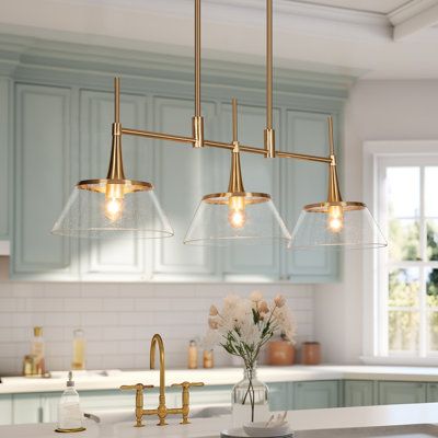 This 3-light linear pendant outfits your kitchen island or dining area with a look that leans heavily on mid-century modern style. Crafted from steel, it features an electroplated brass finish which not only enhances durability but also adds a glamorous look. It includes two height-adjustable rods and a horizontal bar that holds three separate downward-facing fixtures in place. Surrounding each bulb (sold separately) is a clear-seed glass shade that strikes a tapered bowl silhouette, also it fea Brass Kitchen Island, Gold Dining Room, Lights Over Kitchen Island, Gold Light Fixture, Glam Kitchen, Island Light Fixtures, Kitchen Chandelier, Kitchen Island Pendant, Kitchen Island Linear Pendant