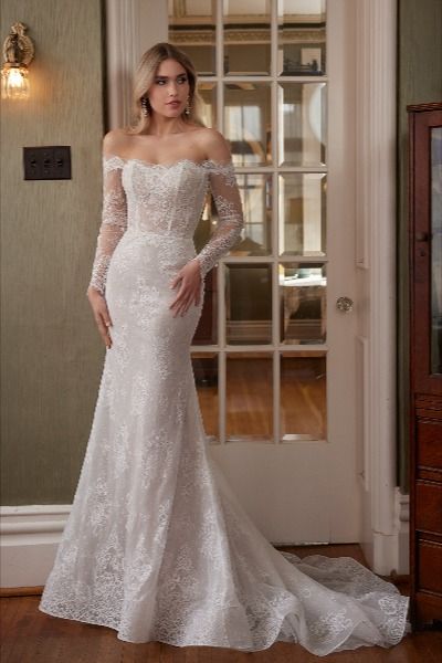 Step into a bygone era of timeless elegance with our vintage-inspired fitted wedding dress, Talisa. Her delicate off-the-shoulder long sleeves evoke a sense of old-world romance, while her exquisite floral lace overlay adds a touch of ethereal beauty to every movement. Designed with a modest straight neckline, this gown exudes grace and sophistication. And with meticulous button details adorning her high back and the cuffs of her long sleeves, the allure of this dress is simply irresistible. Modest Neckline Wedding Dress, Calla Blanche Wedding Dress, Statement Wedding Dress, Calla Blanche, Sheath Wedding Dress Lace, High Neck Wedding Dress, Cape Wedding Dress, Vintage Wedding Dress, Bridal Elegance