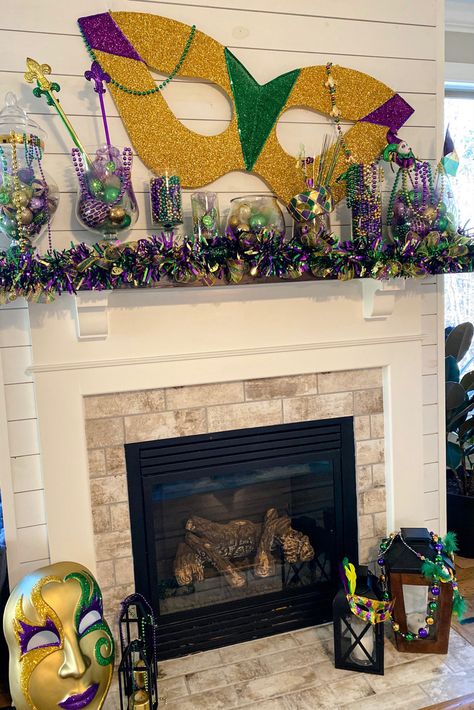 Mardi Gras decorations on mantle using oversized mask, assorted glass containers filled with beads and ornaments in traditional Mardi Gras purple, gold, and green, deco mesh garland, and masks Mardi Gras Garland Mantle, Mardi Gras Christmas Decorations, Mardi Gras Indoor Decorations, Mardi Gras Office Decorations, Mardi Gras Float Ideas Kids, Mardi Gras Mantel Decorations, Mardi Gras Photo Backdrop, Mardi Gras House Decorations, Mardi Gras Parade Float Ideas