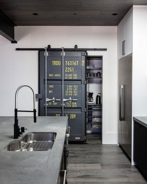 Under a brown plank ceiling, an industrial door on rails opens to a kitchen pantry. Industrial Pantry, Ranch Style House Exterior, Kitchen Pantry Door, Hallway Wall Decor Ideas, Kitchen Pantry Doors, Fireplace Facing, Wood Plank Ceiling, Glass Garage Door, Industrial Door