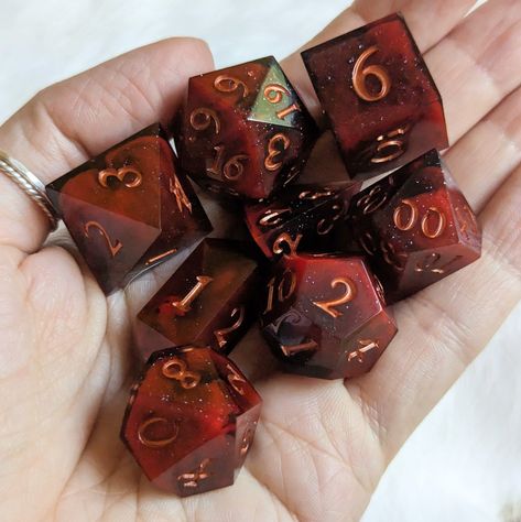 Introducing the "Blood and Smoke" Dice Set, a sharp edge 7-piece polyhedral dice set featuring haunting pools of blood cast in smoky resin, finished with an elegant copper font. Perfect for Dungeons and Dragons and many other exciting tabletop role-playing games, this acrylic set includes one of each: D20, D12, D10, D%, D8, D6, and D4. This Fennek & Finch exclusive is designed by Therin and comes in a cardboard jewelry box with cotton padding for safekeeping. Bring a touch of dark enchantment to Dice Sets Dnd, D&d Props, Clancy Aesthetic, Dnd Dice Aesthetic, Dice Ideas, Cool Dnd Dice, Dice Dragon, Spooky Basket, Dice Goblin