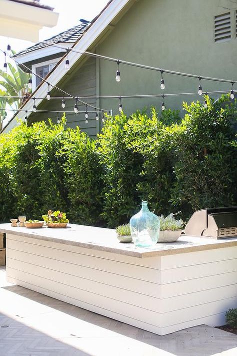 A white shiplap outdoor kitchen is accented with a concrete countertop illuminated by string lights. Shiplap Outdoor Kitchen, Concrete Outdoor Kitchen, Outdoor Kitchen Countertops, Concrete Countertop, Outdoor Kitchen Bars, Kitchen Design Diy, Concrete Kitchen, White Shiplap, Diy Outdoor Kitchen