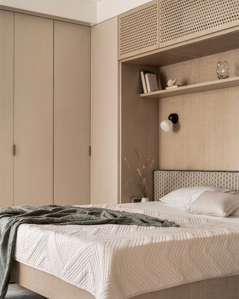 This guest bedroom exudes calm with light-toned finishes, featuring dyed oak wood veneer and beige textured laminate on wardrobes for added depth. The bed is designed to float above the floor, creating openness and maximizing space, while built-in shelves offer extra storage. Perforated shutters neatly conceal the AC unit, keeping the design sleek. A subtle green headboard adds a touch of color, complemented by custom bedside lights and built-in side tables. The paneled TV wall transitions in... Paneled Tv Wall, Wardrobe Above Bed, Built In Bedroom, Bedside Wardrobe, Wardrobe Tv, Green Headboard, Oak Wood Veneer, Bedside Lights, Bedside Lighting