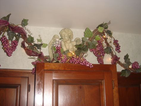 Cherub above a kitchen cabinet with grapevine, purple grapes with ribbon and lights Grape Themed Kitchen, Grape Kitchen Decor, Grape Decor, Tuscan House, Wine Decor, Wine Theme, Purple Grapes, Floral Garland, Kitchen Themes