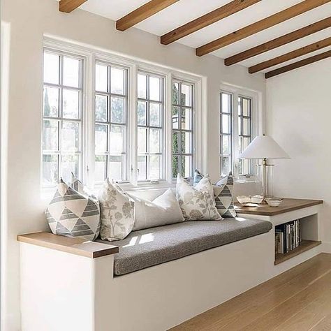 A large white window bench seat layered with accent pillows basks in bright natural light from large windows with a square grid pattern. A lamp with a white shade is placed over a storage area filled with books. White walls brighten the space and light wood flooring runs throughout...   Image: trishaspearsdesign Window Grid Patterns, Window Bench Seat With Storage, Window Bench Seat, Window Seat Kitchen, Window Grids, Window Seat Design, Grid Patterns, Cozy Nooks, Rustic Farmhouse Living Room