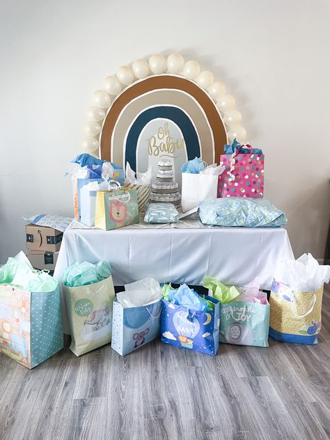 This sweet rainbow themed baby shower with a muted color palette was the perfect way to welcome baby. The gift table is pictured here with a plywood hand painted rainbow backdrop, balloon border, and diaper cake centerpiece. Pampas grass floral arrangements and framed maternity photos complete the look. Rainbow Baby Shower Ideas For Boys, Rainbow Baby Shower Centerpieces, Blue Rainbow Baby Shower Ideas, Boy Rainbow Baby Shower Ideas, Muted Rainbow Baby Shower Ideas, Neutral Rainbow Baby Shower Ideas, Rainbow Baby Shower Ideas Decoration, Rainbow Themed Baby Shower Ideas, Centerpiece Pampas