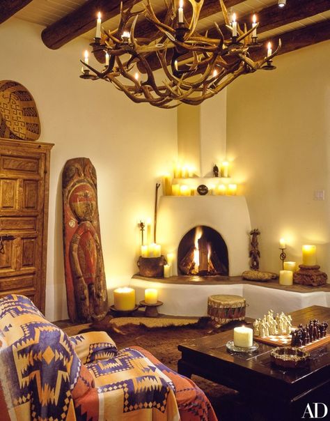 In the living room, a carved and painted totem from New Guinea rests beside the kiva-style fireplace. Atop the armoire is a Papago cradle basket. The Mexican church candles throughout were made especially for Kent’s shop. Santa Fe Interior Design, Santa Fe Style Decor, Southwest Interior Design, Santa Fe Interiors, Southwest Interior, Western Interior Design, Santa Fe Decor, Santa Fe Style Homes, Southwest Home Decor