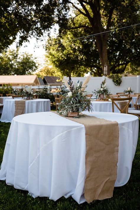 White tablecloths are decorated with beige table runners and floral arrangements in a Chico, CA backyard wedding White Tablecloth With Burlap Runner, Beige And White Decor Party, Burlap And Lace Table Decor, Wedding Table Covers Ideas Tablecloths, Reception Table Cloth Ideas, White Table Clothes Wedding, White And Wood Party Decor, Round Party Tables, White Table Cloth With Burlap Runner