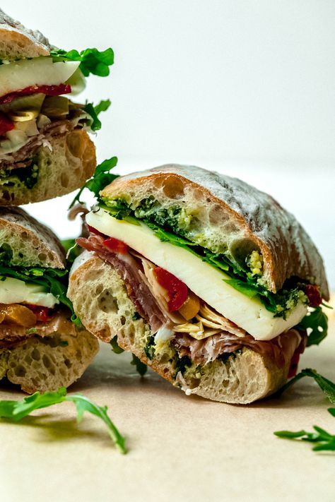 Antipasto Sandwich with Lemon-Basil Pesto | All of your favorite flavors from an antipasto board, all wrapped up in sandwich form!  Layers of lemony basil pesto, salami, prosciutto, mozzarella and provolone cheeses, arugula, artichokes and hot and sweet roasted peppers make this burst with flavor.  Make in advance and let the flavors get to know each other in the fridge-then eat this cold, at room temperature or hot as a pressed sandwich!   #food #recipe #antipasto #lunchideas #sandwichrecipes Shower Sandwiches, Antipasto Board, Lemon Basil Pesto, Hiking Lunch, Prosciutto Mozzarella, Lunch Sandwiches, Captain Crunch, Pressed Sandwich, Not Hungry