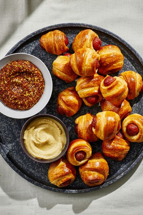 Making the iconic crowd-pleaser doesn’t get easier than with this recipe of mini smoked cocktail sausages (or petit hot dogs) wrapped in store-bought buttery pastry. Prepared crescent roll dough does a lot of heavy lifting here, but you can use puff pastry if you prefer. Served as part of a full-out spread for the Super Bowl, a Monday game day, holiday fête, or weekend get-together, this classic party appetizer will likely disappear as quickly as you put it out, so be prepared to make plenty. Sausage In Pastry, Mini Weiner Appetizers, Mini Hot Dogs In Crescent Rolls, Puff Pastry Hot Dog, Sausage Puff Pastry, Sausage Pastry, Easy Pigs In A Blanket, Mini Pigs In A Blanket, Mini Hotdogs