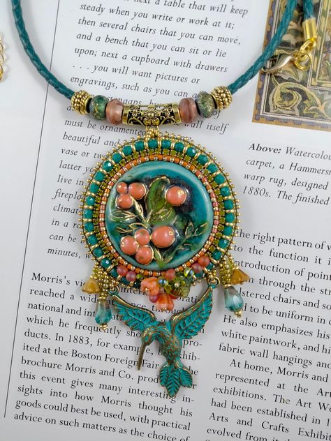 This beautiful ceramic cabochon with Lingonberries has wonderful detail and colours of turquoise, green gold and a very soft peach. I have surrounded the cab with pale peach beads, acid green crystal cup chain and turquoise fire polish beads. Pretty flower beads and drops decorate the section above the hanging Hummingbird which is verdigris metal. The two dangles on either side are drop and flower beads. The pendant measures 10cms ( 4 inches )  from the bottom tip of the Hummingbird tail feather Embroidery Pendants, Bead Embroidered Pendant, Embroidered Pendant, Hippy Gifts, Pale Peach, Bead Embroidery Patterns, Tail Feathers, Pretty Flower, Flower Beads