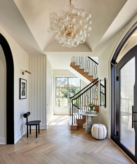 Herringbone-patterned wood flooring infuses a Parisian vibe into the foyer of this Winnetka dwelling, while fluted wall paneling by Wood & Art and a Visual Comfort & Co. chandelier add drama. A Soho Home stool is paired with a CB2 table. Staircase Landing Ideas, Landing Ideas, Staircase Landing, Upholstered Wall Panels, Venetian Plaster Walls, Built In Banquette, Three Season Room, Herringbone Wood Floor, Herringbone Wood