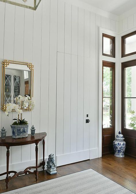 Cottage entry features a jib door with vertical shiplap trim and a gold leaf Greek key mirror over a demilune console table. Hidden Shiplap Door, Shiplap Hallway, Jib Doors, Jib Door, Dark Stained Wood Floors, Blue Chinoiserie Wallpaper, Shiplap Trim, Bath Goals, Black Floral Wallpaper