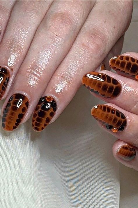 These oval-shaped Crocodile Nails are a bold statement. The rich brown base features an intricate black scale pattern, creating a realistic crocodile skin effect. Some nails are accented with small, colorful gems for a touch of glamour. Perfect for those wanting a wild and chic look!  // Photo Credit: Instagram @doneupbytiffany Crocodile Nails, Sophisticated Manicure, Es Nails, Oval Shaped Nails, Scale Pattern, Coffin Shape Nails, Crocodile Skin, Oval Nails, Wild Child