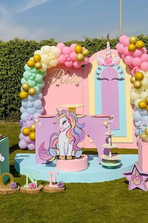 Colorful birthday party setup with a unicorn theme, featuring balloons, a cake, and a large unicorn cutout decoration in a garden. Unicorn Themed Birthday Party Diy, Unicorn Party Theme, Magical Unicorn Birthday Party, Unicorn Party Ideas, Unicorn Birthday Party Ideas, Whimsical Decorations, Fairytale Land, Unicorn Balloons, Unicorn Party Food