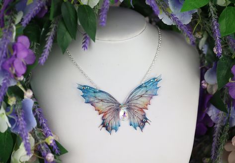 A must-have for all fairies! A unique and truly beautiful transparent blue/gold fairy wing pendant. This necklace is embellished with silver sparkle, gems and a silver key charm. The wings measure approximately 10cm across. This delicate array of fairy wings is really rather lovely. It is perfect for all fairy lovers - whether to be worn as part of a costume, or simply as a pendant for everyday wear. It is super light weight, and the wings are slightly flexible to touch. These wings are far more durable than their glassy appearance might suggest! Please note that the wings may grow cloudy over time when exposed to sunlight, heat, perspiration and makeup. The wings should also avoid contact with water. Please store carefully when not wearing, away from direct sunlight. The chain measures ap Fairy Jewellery, Fantasy Crown, Handmade Fairy, Wing Jewelry, Fairy Gifts, Cottagecore Fairy, Fairy Jewelry, Blue Fairy, Fairycore Cottagecore