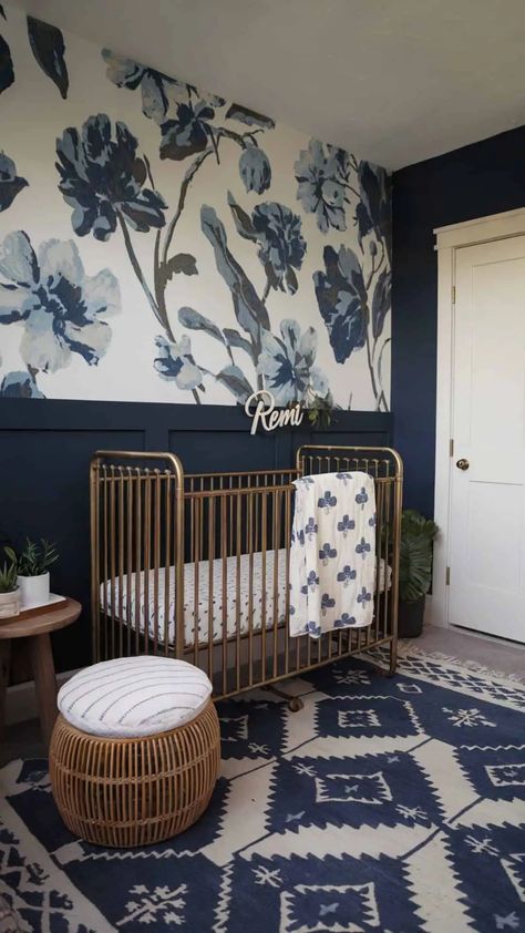 Navy and white nursery with bold floral wallpaper, a gold crib, and rattan pouf, accented by personalized decor. Navy Blue Nursery Girl, Blue Girl Nursery Ideas, Dark Blue Nursery Ideas, Nursery Blue Walls, Dark Floral Nursery, Panelled Nursery, Navy And Gold Nursery, Nursery Murals Painted, Bold Nursery Ideas