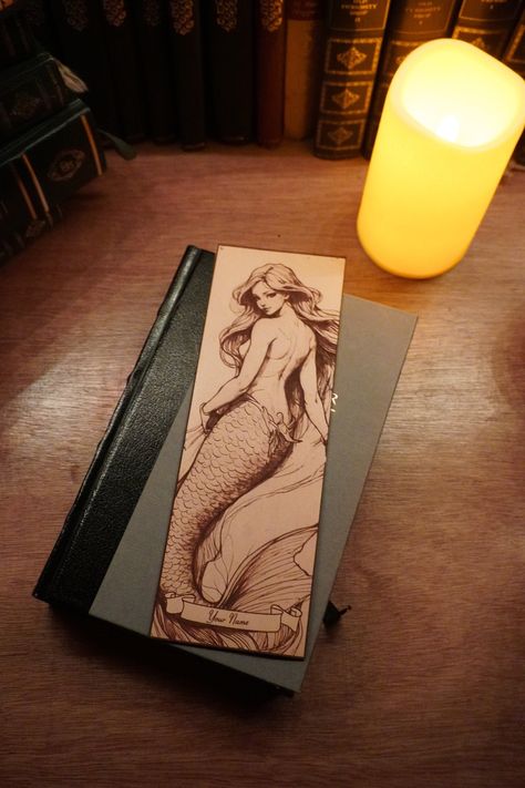 Oversized leather bookmark with a laser etched image of a Mermaid sitting on a closed book on a desk with a candle Drawn Bookmarks, Ethereal Mermaid, Mermaid Bookmark, Mermaid Design, Reading Adventure, Leather Bookmark, Functional Art, Book Accessories, Book Worms