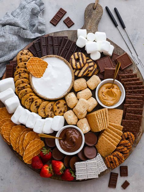 Just in time for summer barbecues and camping trips, this s'mores charcuterie board is here to sweeten things up! It features a mix of different types of chocolate, crackers, marshmallows, and spreads so everyone in your family can create their own perfect sweet treat. Camp Theme Charcuterie Board, Halloween S’more Charcuterie Board, Smores Dessert Board, S'more Platter, S’more’s Charcuterie Board, S’mores Ornament Diy, S’mores Charcuterie Boards, Charcuterie Board Popcorn, Bonfire Charcuterie Board