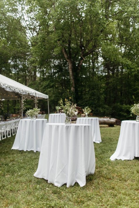 Five cocktail tables with white tablecloths and vases with flowers. Outdoor Wedding Cocktail Tables, Garden Party Wedding Cocktail Hour, Simple Cocktail Hour Decor, Lawn Cocktail Hour Wedding, Cocktail Reception Wedding Layout, Cocktail Wedding Layout, Diy Backyard Wedding Reception, Outdoor Wedding Cocktail Hour Decor, Backyard Wedding Cocktail Hour