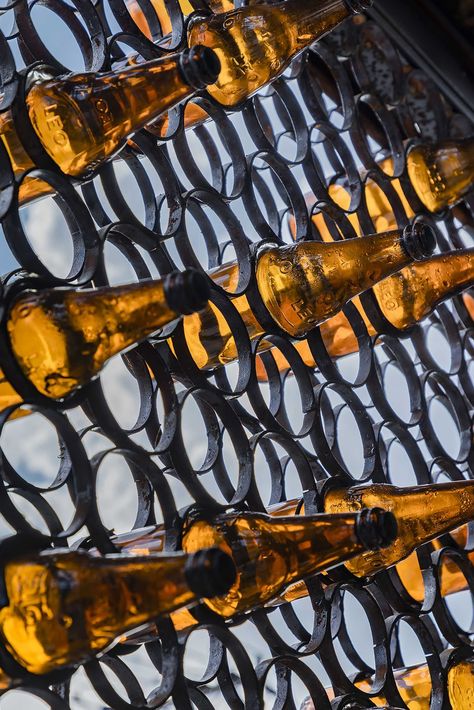 A modern cafe with a facade that features metal rings that hold recycled beer bottles. Wood Banquette, Brick Tile Floor, Recycled Beer Bottles, Recycle Metal, Small Seating Area, Big Families, Hidden Lighting, Wood Facade, Warm Color Schemes