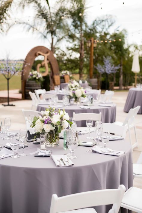 Wedding table centerpieces, flowers with gray tablecloths, Hanford Ranch Winery, Galt, CA Lavender Table Cloth Wedding, Lavender Tablecloth Wedding, Lavender Wedding Table Decorations, Lavender And Sage Wedding Table Settings, Purple And Lilac Table Setting, Light Purple Wedding Table Decor, Wedding Centerpieces Lavender Color, Lilac And Silver Table Decorations, Purple Wedding Round Table Settings