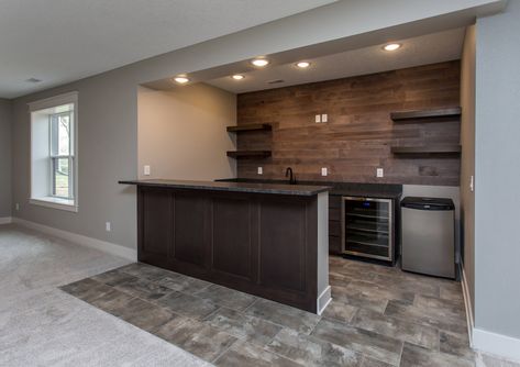 Basement bar in this modern Rustic Farmhouse! Wood wall with floating shelves and a wine cooler built in. All paired with gray rustic tiles for a rustic farmhouse feel! Tour this home by following the link in the bio! Rustic Farmhouse Basement, Farmhouse Basement Bar, Bar With Floating Shelves, Farmhouse Basement, Basement Remodel Ideas, Wet Bar Basement, Basement Bar Plans, Basement Bar Design, Basement Bar Ideas