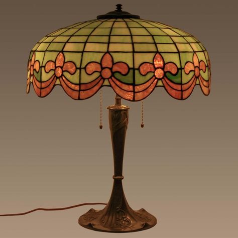 Antique American bronze and leaded glass table lamp by Wilkinson, circa 1910. The three light lamp having a dome shaped shade with striated leaded glass green & ivory tiles and having amber colored Fleur-de-Lis & swagged garland decoration to the base of the shade. The lamp is raised on the original bronze base decorated in an organic Art Nouveau design. The lamp is in very good condition and has been sympathetically rewired with period style materials, creates a warm pleasant light.  Bloomsbury Lampe Art Nouveau, 1930s Lamp, 1920s Lamp, Fancy Lamp, Minecraft Torch, Ill Wait, Art Nouveau Lamp, Eclectic Lamps, 70s Lamp