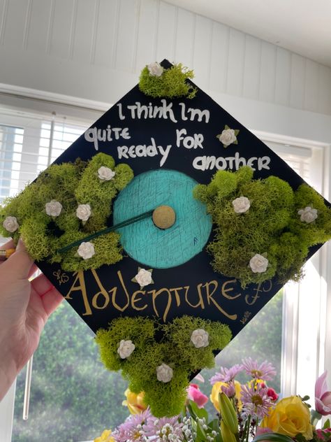 A black graduation cap with moss and little white flowers surrounds a blue door that resembles a "Hobbit door" from The Hobbit and the Lord of the Rings movies, with a quote around the door saying "I think I'm quite ready for another adventure." Anne Of Green Gables Graduation Cap, Lotr Graduation Party, Lotr Graduation Cap, Lord Of The Rings Graduation Cap, Lotr Tattoo, College Grad Cap Ideas, Graduation Cap Decoration Diy, High School Graduation Cap, College Graduation Cap Decoration