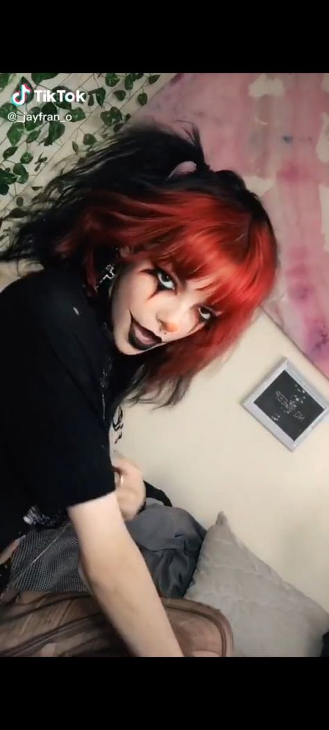 A person sitting on their bed with red and black hair in pigtails, a black short sleeve top and distressed tights. The person has red and black clown makeup with black lips and eyeliner. Clown Hairstyles Halloween, Cute Clown Makeup Red And Black, Clown Makeup Black And Red, Christmas Clown Makeup, Red And Black Jester Makeup, Red And Black Clown Makeup, Clown Eyeliner, Red Black And White Clown Makeup, Red Clown Makeup