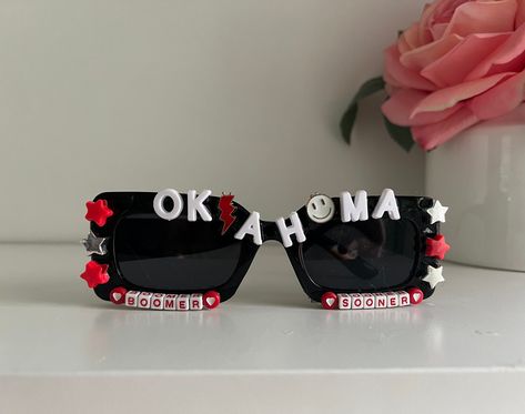 "Boomer Sooners! Football Season is just around the corner and how PERFECT are these for tailgating and football games! You are sure to be noticed on game day!  These sunglasses are a retro black rectangle that say \"Oklahoma\" in large white  letters with red and white stars along the side of the frames. The bottoms say Boomer Sooners Are you looking for the perfect one of a kind gift for a past, current or future OU fan that won't break the bank? Are you trying to up your game day fit to the n Graduation Sunglasses, College Bed Party, College Spirit Wear, Black Rectangle Sunglasses, College Bed, High School Grad Gifts, Bed Party, Childrens Glasses, Graduation Party Gifts