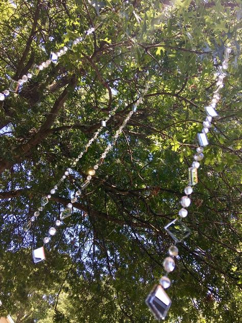 These are crystal-clear rhinestone strings of tree jewelry.  The mirrors and clear rhinestones maximize the reflection of the sun, moon, street lights ... and it's just magical!  Take a look at the video to see the reflective lights that dance around!!Fancy Tree Jewelry adds whimsy and fun to any outdoor space year round! Everyone loves the tiny reflections and the bursts of sparkle that scatter and dance when the wind catches and the sun or moon is shining. Tough enough to withstand summer heat Ornaments Hanging From Outdoor Tree, Crystals Hanging From Trees, Yard Tree Decorating Ideas, Tree Charms Backyards, Hanging Garden Decor, Whimsical Outdoor Decor, Boho Garden Ideas Diy, Garden Art Diy Whimsical, Enchanted Garden Backyard