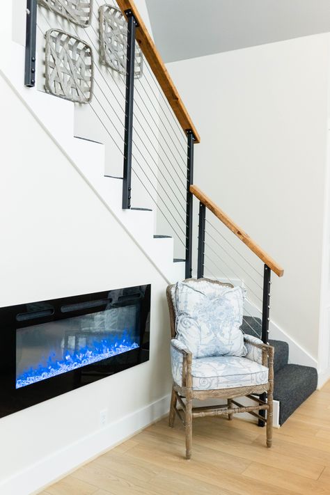 Modern wire and wood stair rail eith electic fireplace. A-frane stairs and living room. Electric Fireplace Under Stairs, Under Stairs Fireplace, Fireplace Under Stairs, Electic Fireplace, Stairs And Living Room, Unique Cabin, Electric Fireplace Living Room, Modern A Frame, Stair Rail