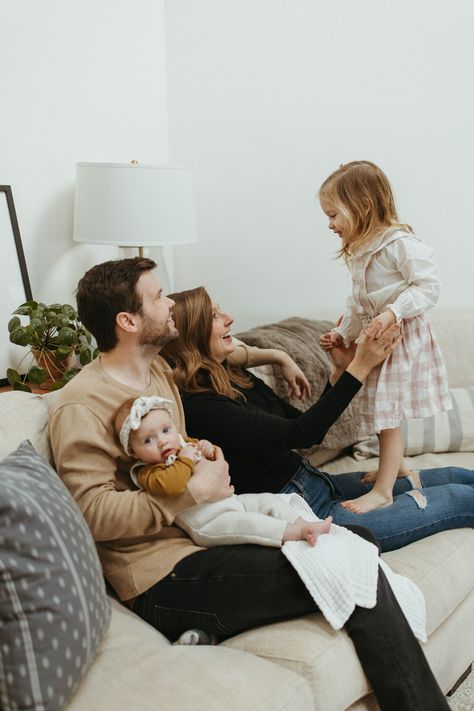 photo is a family photo of a 4 year old standing on her mother's lap and a 4 month old baby sitting on her father's lap on a cream colored couch with throw pillows Lifestyle Session Family, Family Of 4 In Home Session, Family Inhome Session, Family Home Session, Family Session Ideas, Home Family Session, Indoor Family Photos, Family Newborn Photography, Lifestyle Family Photos