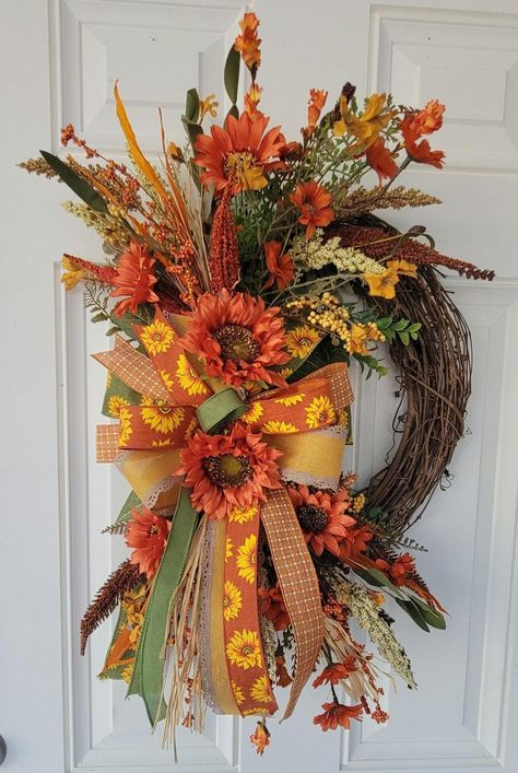 Welcome the beauty of autumn with our Handmade Fall Harvest Floral Wreath, a stunning addition to your seasonal decor. This exquisite wreath features a vibrant arrangement of sunflowers, orange blossoms, and lush greenery, all complemented by elegant ribbons in warm fall colors.  Measures 28"L x 19"W, perfect for your front door. This wreath will create a welcoming atmosphere for guests and bring the festive spirit of the harvest season to your home.        This Fall Harvest Wreath is not just for your front door, it also makes a lovely centerpiece for your dining table, a charming decoration for your fireplace mantel, or a thoughtful gift for friends and family during the Thanksgiving season.          Add a touch of rustic elegance and the warmth of the harvest season to your home this be Fall Wreaths For Front Door Autumn, Fall Wreaths With Sunflowers, Fall Grapevine Wreath Ideas, Welcome Fall Wreath, Autumn Front Door Decor, Sunflower Fall Wreath, Fall Wreath With Sunflowers, Grapevine Fall Wreath, Fall Floral Door Swags