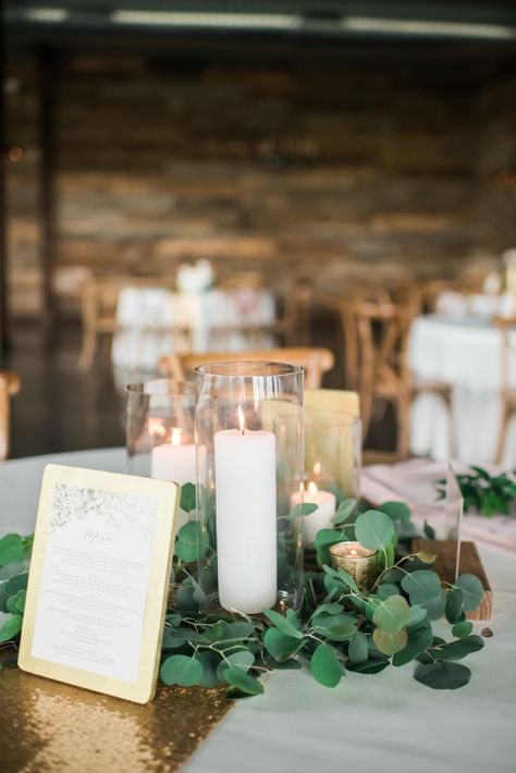 Candle centerpiece on a bed of eucalyptus. Table Centerpieces Eucalyptus, Wedding Table Decor Eucalyptus, Eucalyptus Centerpiece Wedding, Centerpiece Wedding Candles, Eucalyptus And Candles, Table Decor Eucalyptus, Centerpieces Eucalyptus, Eucalyptus Centerpiece, Wedding Candles Table