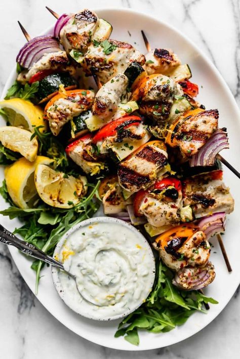 Photo of Greek Chicken Kebabs with Tzatziki Sauce on a serve platter with arugula, grilled lemons and a bowl to Tzatziki sauce. Greek Chicken Kebabs, Greek Chicken Kabobs, Weekend Meal Prep, Tzatziki Sauce Recipe, Dorito Casserole, Real Food Dietitians, Greek Foods, Greek Flavors, Chicken Kebabs