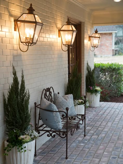 Show hosts Chip and Joanna Gaines knew that a front porch would really make this house a home. By extending the roofline, they were able to create this breezeway porch with vintage light sconces and an ornate wrought-iron bench. French Country Front Porch, Painted Brick House, Beautiful Exterior, Hgtv Fixer Upper, Lighting Garden, Magnolia Farms, Brick Flooring, Garden Light, Design Seeds