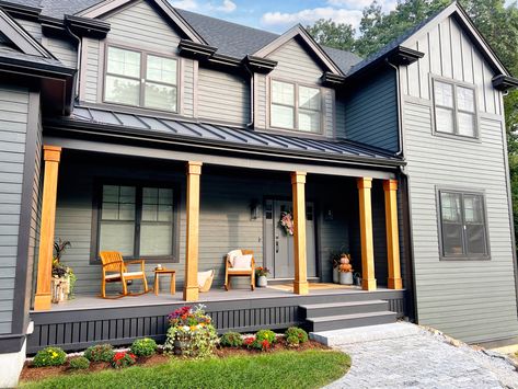 Fall 2023 dark gray modern house ideas: a large front porch supported by cedar columns, exterior wainscoting siding, and black exterior trim. This moody house design is perfect for fall, decorated with lots of neutrals, natural tones, and texture. Fall planters, rocking chairs, layered rugs, and a pumpkin wreath for the front door. #darkexterior #modernhouseexterior #fallfrontporch #outdoorfalldecor #moodyhome #blackhouse Cedar Posts Front Porch Gray House, Dark Gray House With Wood Accents, Cedar Posts Front Porch, Cedar Front Porch, Black Exterior Trim, Exterior Wainscoting, Cedar Columns, Porch Building, Front Porch Pillars