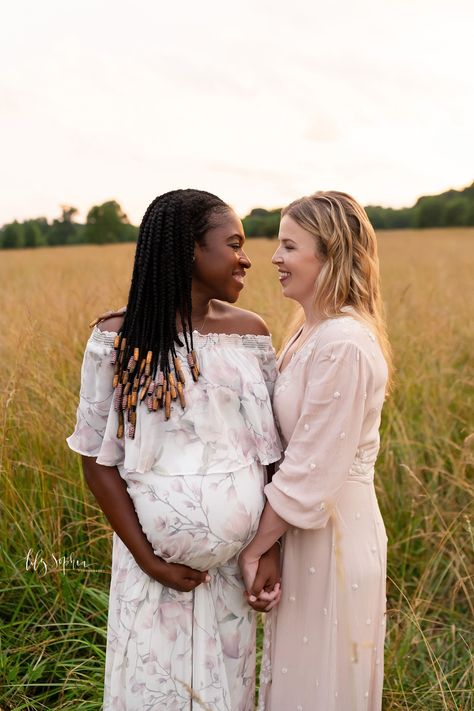 Two married women in beautiful dresses expecting a baby hold hands and smile at each other as they stand in a field at sunset during a Maternity Session by Lily Sophia Photography near Atlanta, Georgia #lilysophiaphotography Maternity Photography Lesbian Couple, Wlw Pregnancy Aesthetic, Lesbian Maternity Photos, Lesbian Family Photos With Baby, Surrogacy Pictures, Lesbian Maternity Photoshoot, Lesbian Family Photos, Field At Sunset, Pregnancy Belly Photos