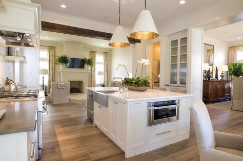 Welcoming white kitchen features a white island fitted with a stainless steel microwave, stainless steel stacked dishwasher and a stainless steel dual apron sink paired with a polished nickel faucet fixed to a white marble countertop lit by Two Goodman Hanging Lamps. Island With Sink And Dishwasher, Kitchen Island With Sink And Dishwasher, Stainless Steel Apron Sink, Island With Sink, Sink And Dishwasher, Functional Kitchen Island, Kitchen Island With Sink, Unique Kitchen Design, Best Kitchen Sinks