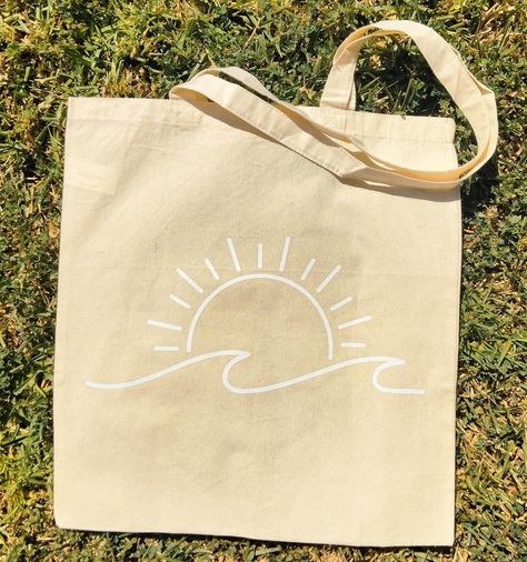 "Our Minimalist Styled Beach Summer tote bag is a must have summer essential!  This beige tote bag  is designed with a white minimalist print of a sun and a beach wave.  Our bag is a great way to carry your belongings when you are at the beach, on vacation ; or just going out for the day.    This eco friendly bag is re-usable and made from 100%  cotton. PRODUCT DETAILS: -Dimensions - 15\"W x 16\"H inches -100% cotton lightweight medium tote bag -One-sided tote design -Each tote bag is handmade, so there may be variations from tote to tote." Beach Bags Totes Diy, Simple Tote Bag Design Paint, Cute Bag Designs, Tote Bag Summer Design, Tote Bag Painting Ideas Beach, Cricut Aesthetic Ideas, Cute Tote Bags Design, Paint Tote Bag Ideas Easy, Cute Tote Bag Ideas